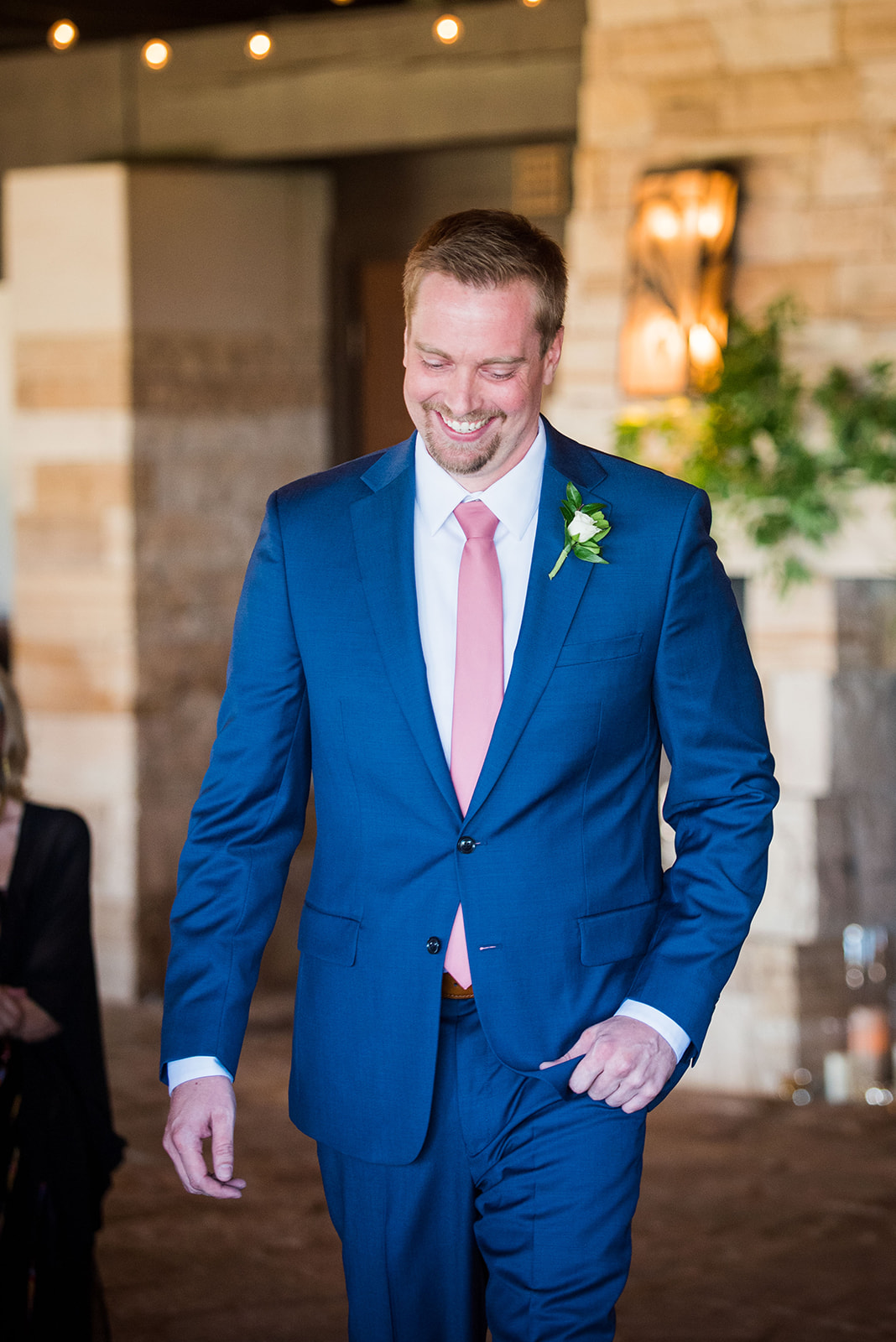The groom smiles down at the ground as he walks up the aisle during the wedding ceremony.