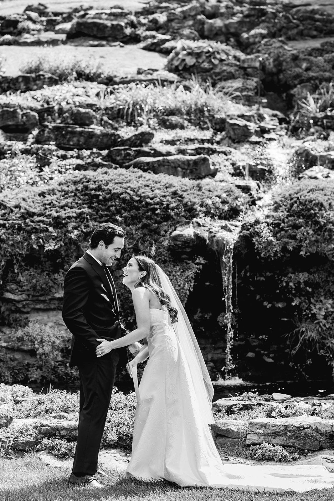 Black and white photo of bride and groom laughing in front of waterfall at Country Club of Buffalo.