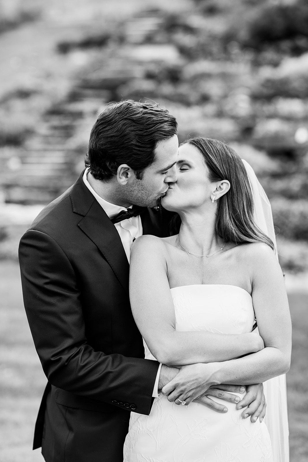 Black and white photo of bride and groom nestles in for a kiss in front of waterfall at Country Club of Buffalo.