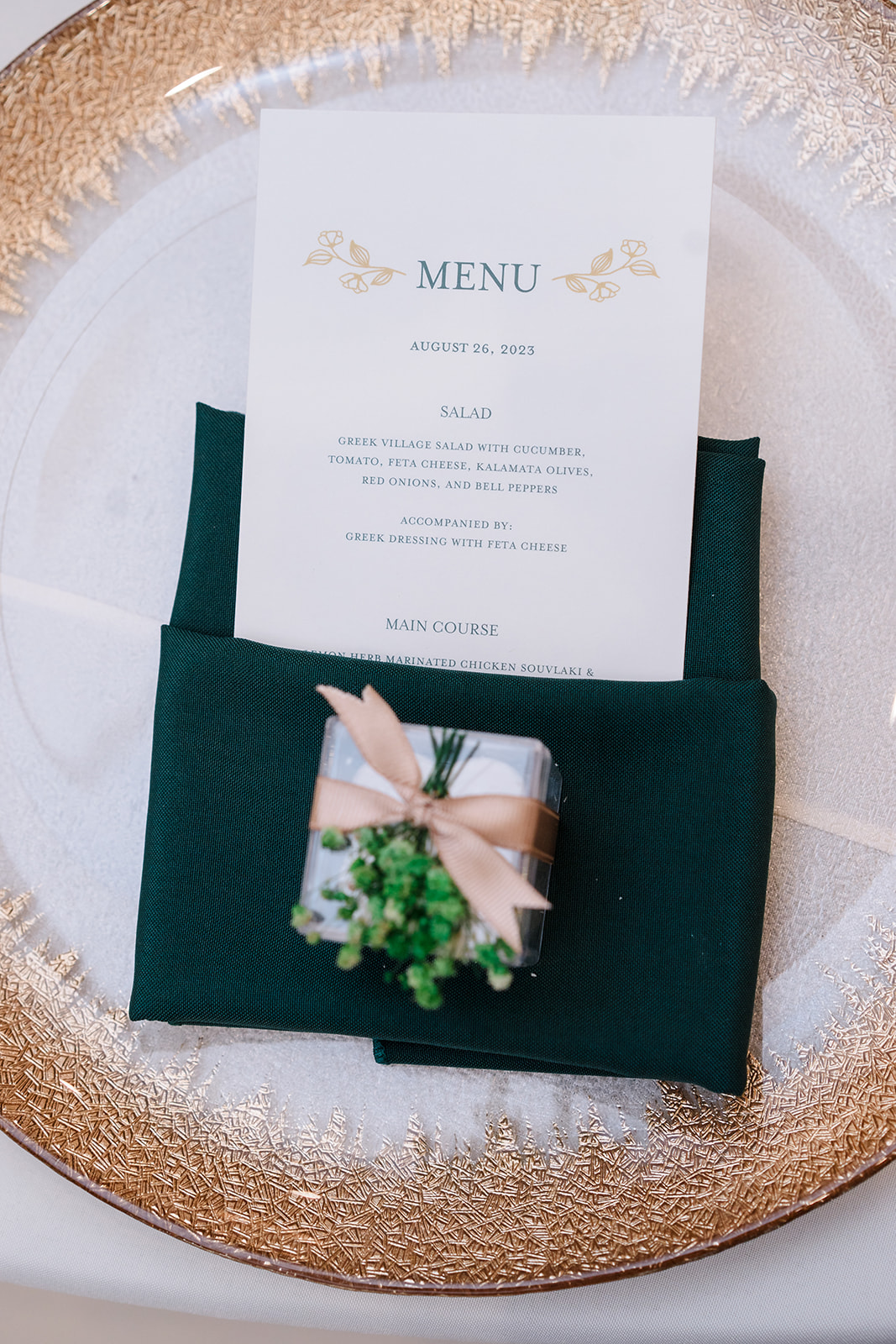 Reception menu card in green napkin on a gold-rimmed charger plate.