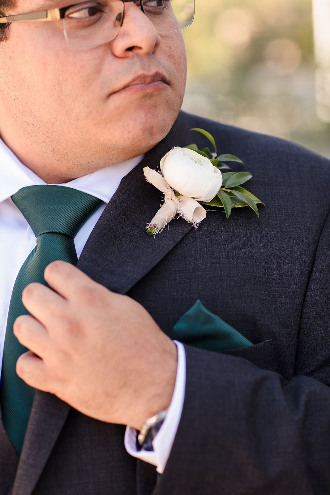 Groom has dark green tie and white floral boutinnere