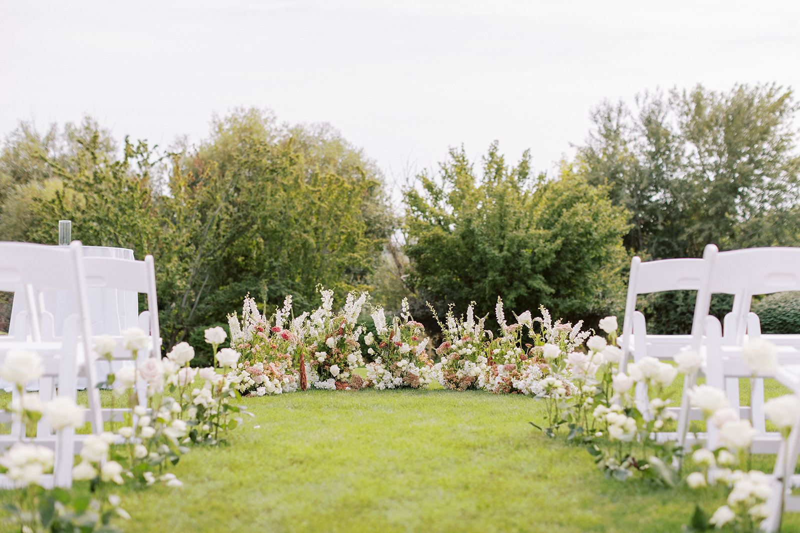 Ceremony site with white roses lining the aisle and a mix of summer blooms as a backdrop for the couple.