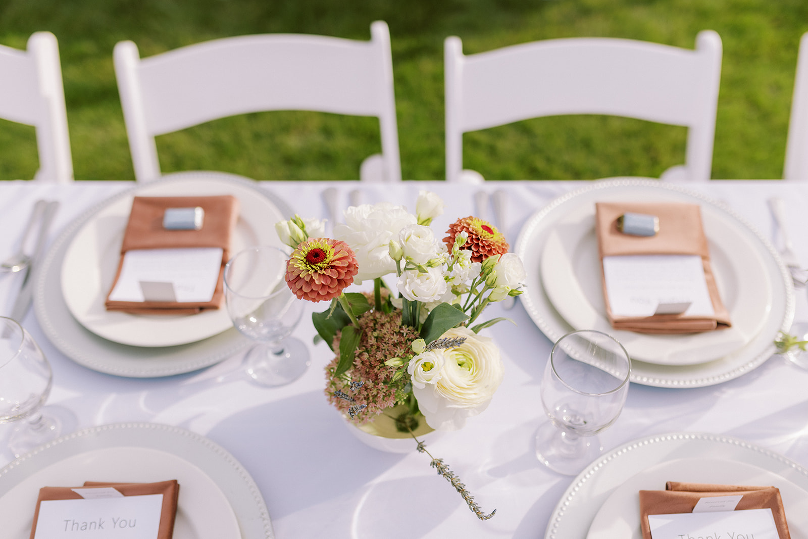 Clean white linens and and plates with summer floral arrangements down the center of the long reception tables.