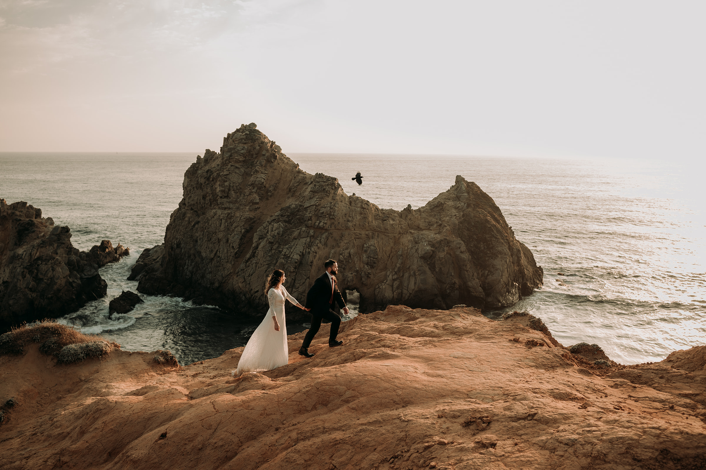Bride and groom running on cliffs in Big Sur California 