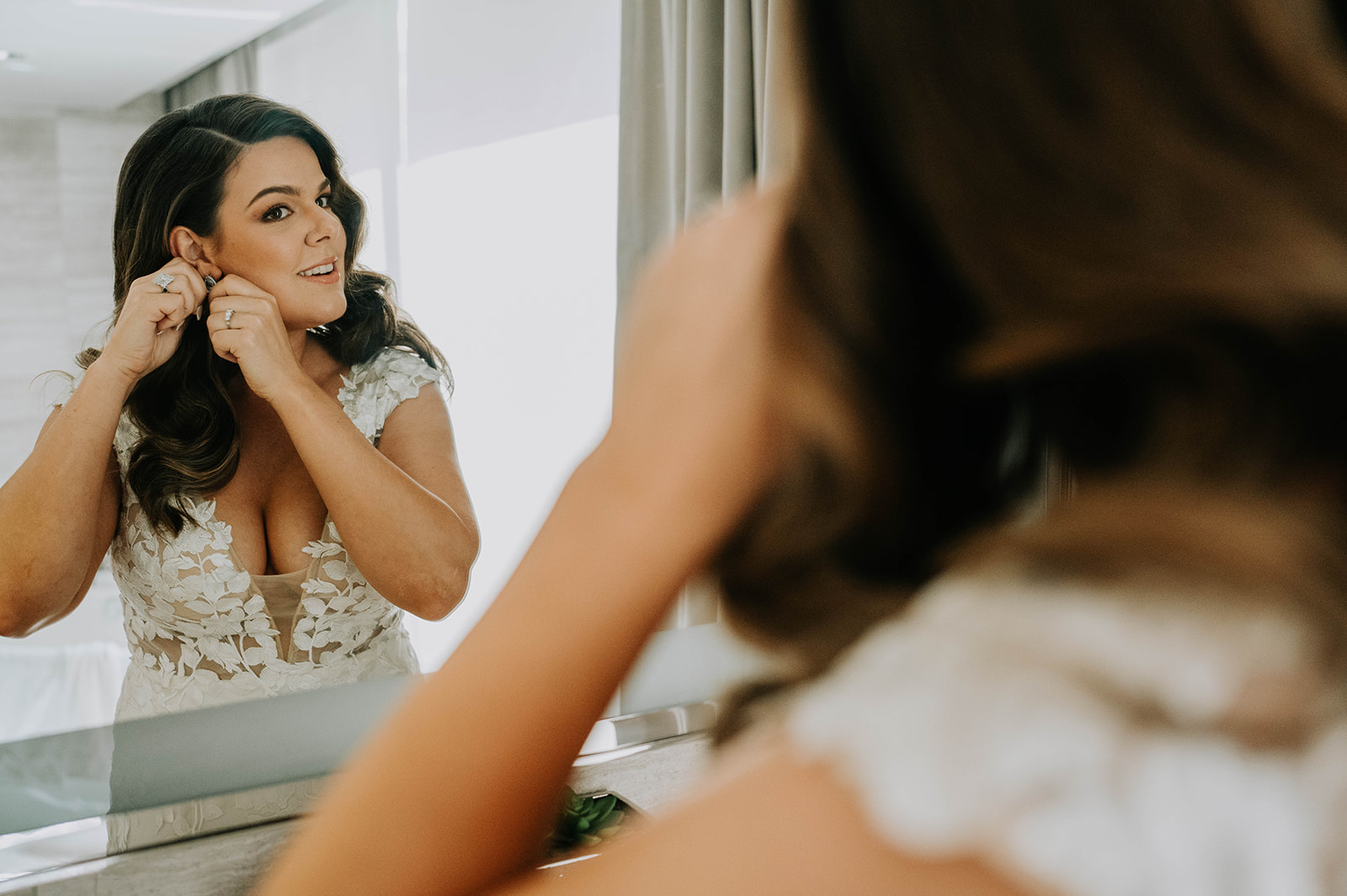 bride putting on earrings in the mirror