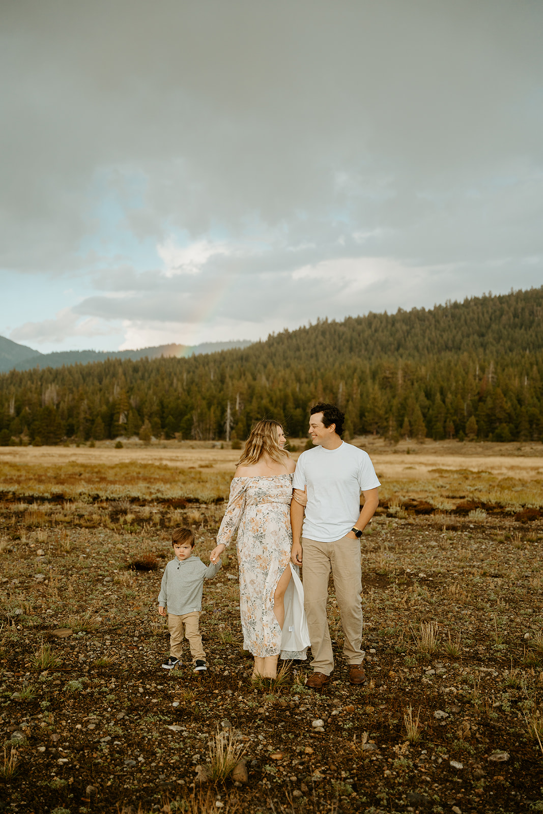A family walking through a field for during fall after a swift rainstorm for their maternity photos in Hope Valley, CA.