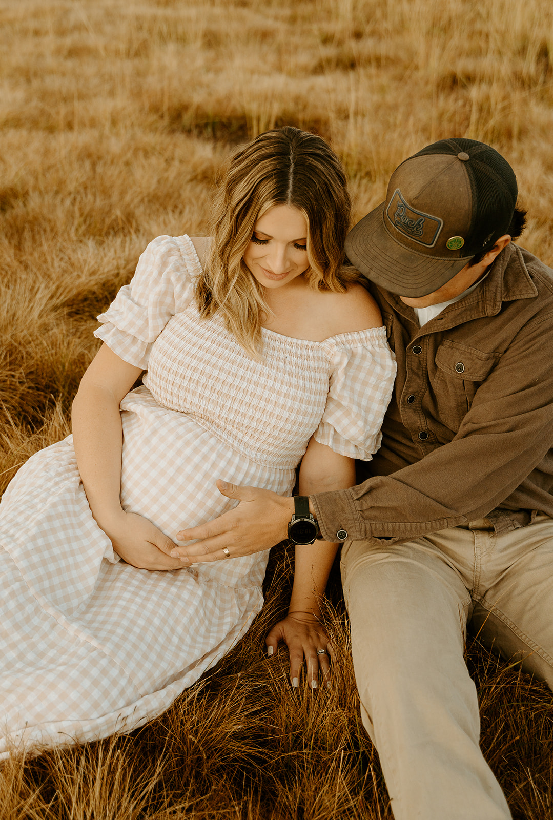 a romantic portrait of a couple snuggled up in a field during their maternity photoshoot. 