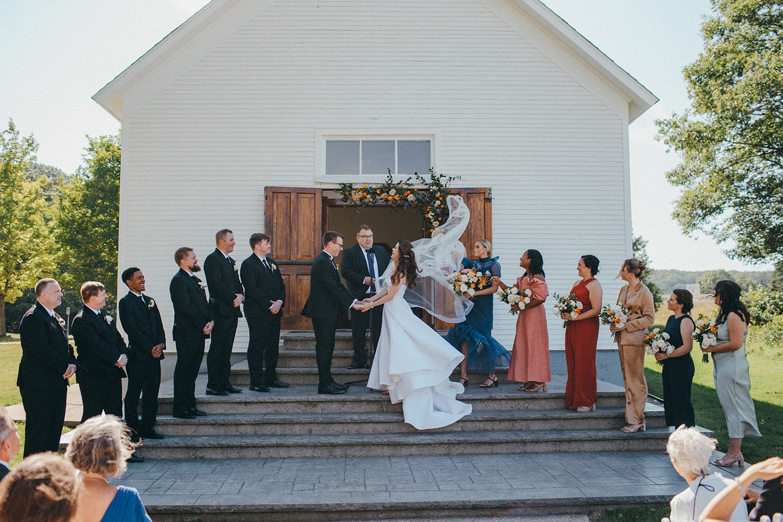 A bride and groom get married on the front steps of a little white chapel at the Felt Estate in Saugatuck, Michigan