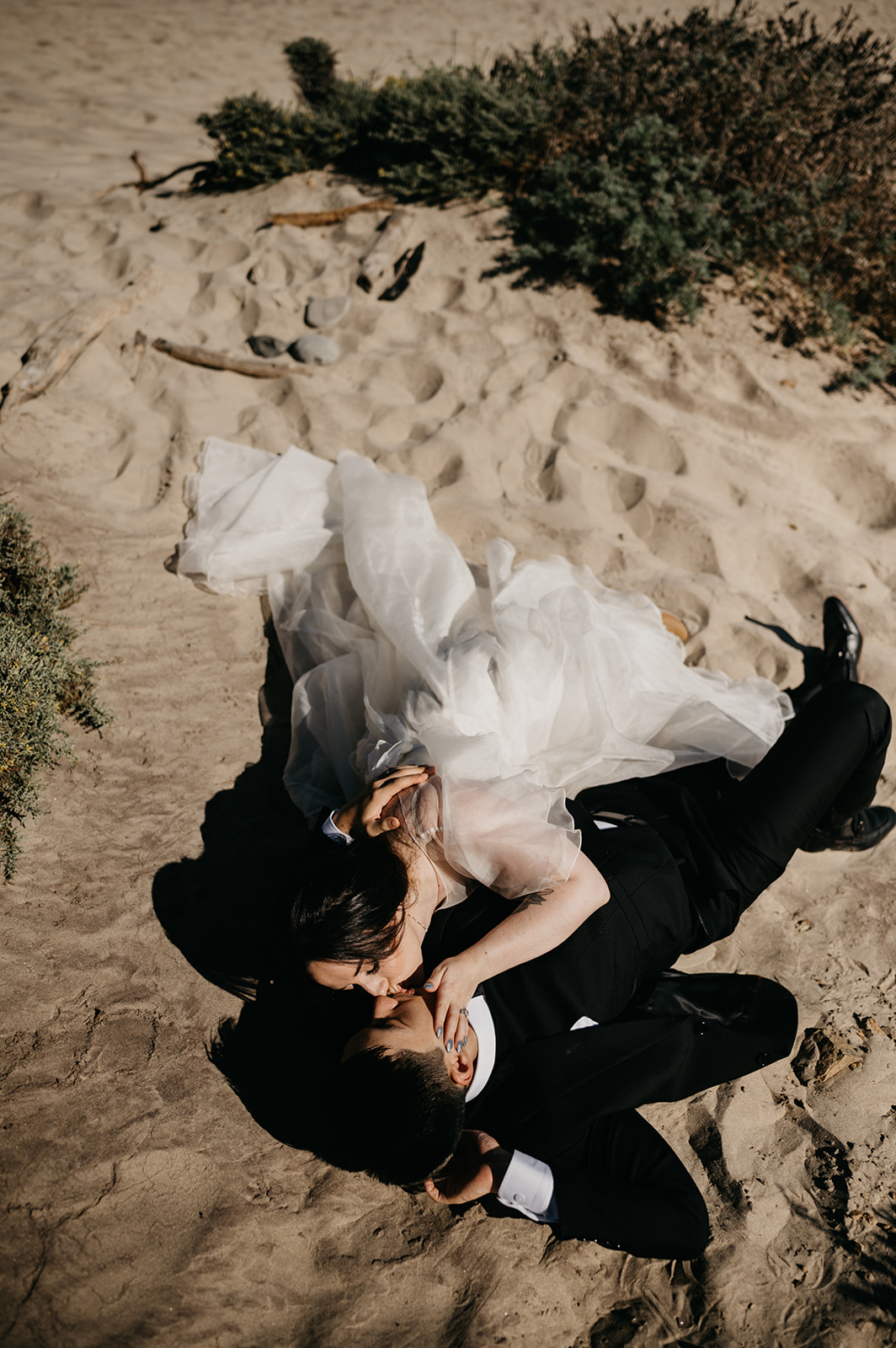 Bride and Groom laying in the warm sand at the beach in Big Sur California embracing each other.