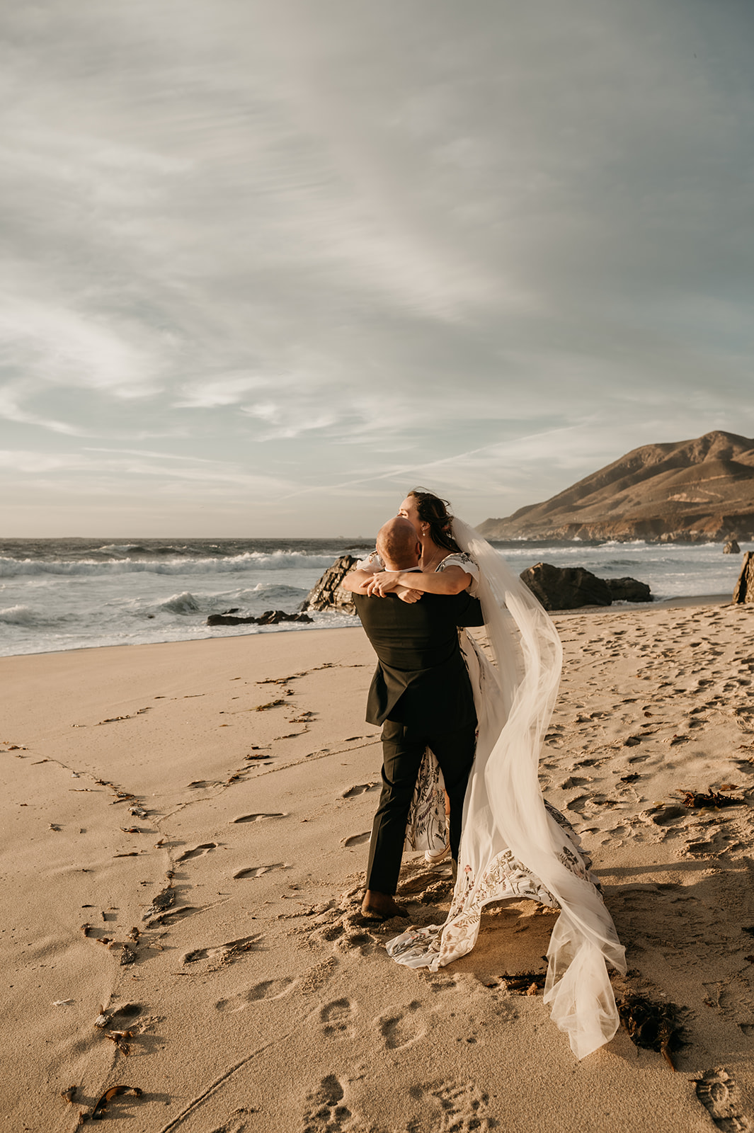 Groom carrying bride on beach at Big Sur California