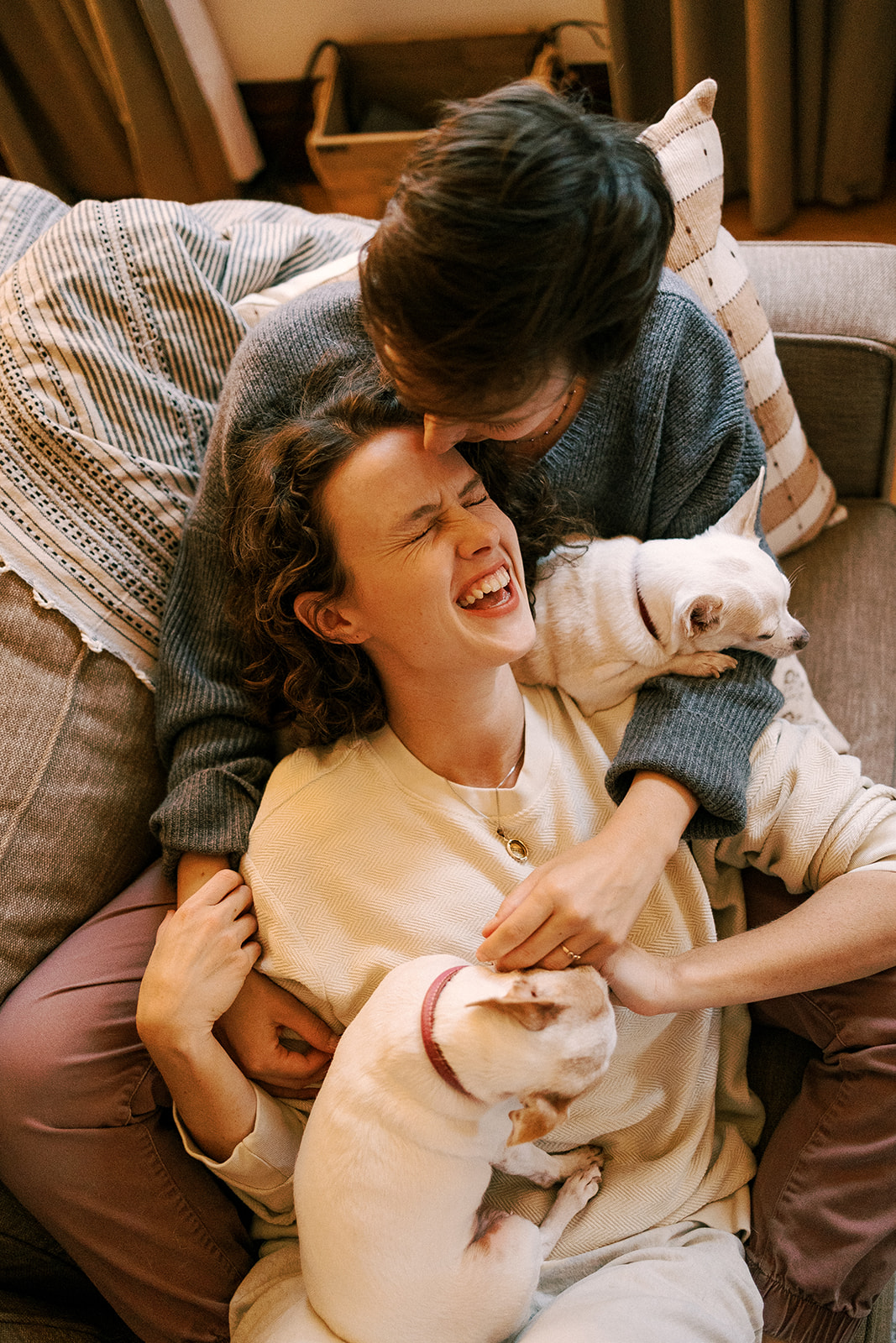 couple cuddles on their couch with their dogs and laughs