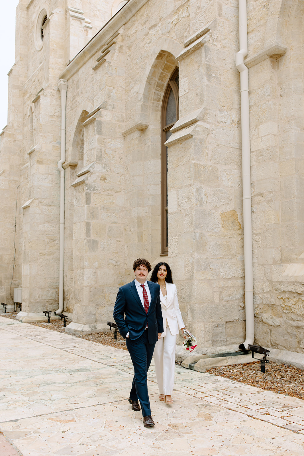Bride and groom walk in front of a large church