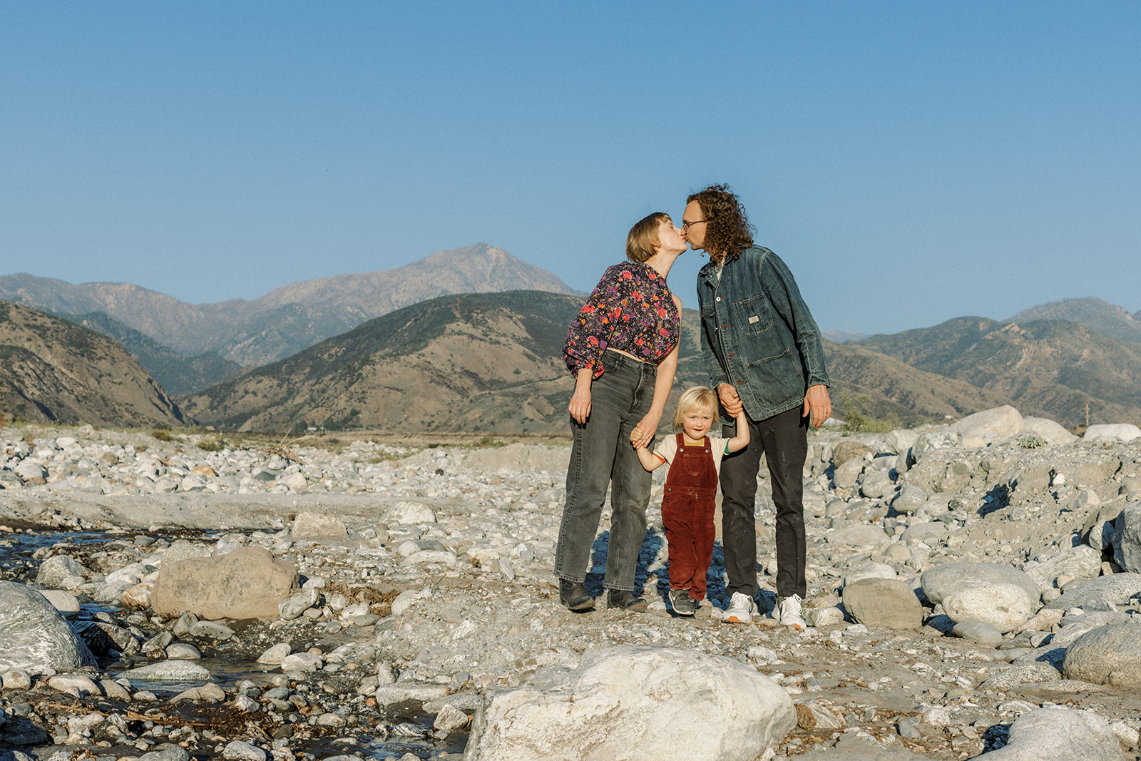 Family of three standing in dry riverbed with San Bernardino mountains behind them.
