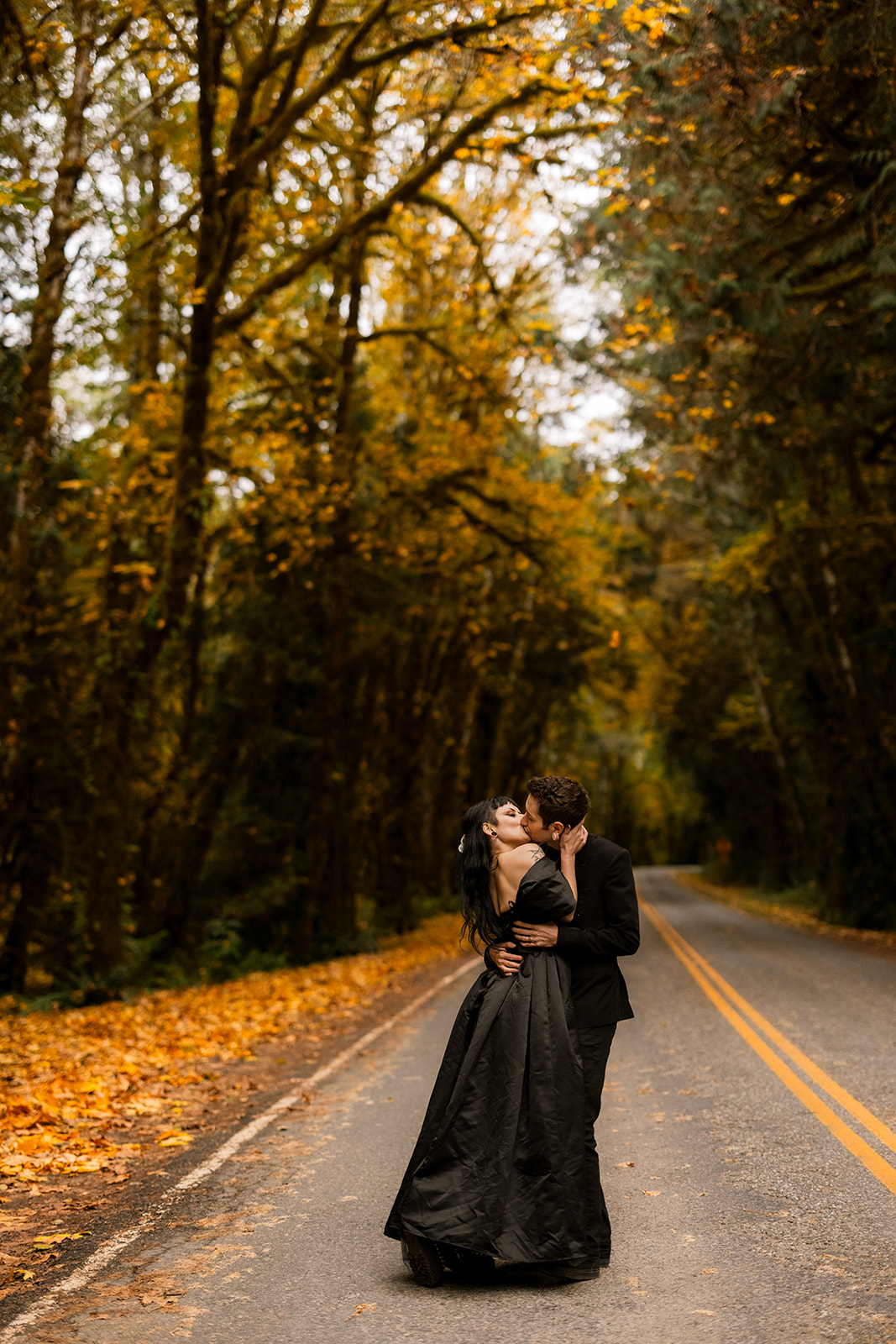 A couple shares an intimate kiss while standing in the road in the Hoh Rainforest on a fall day.