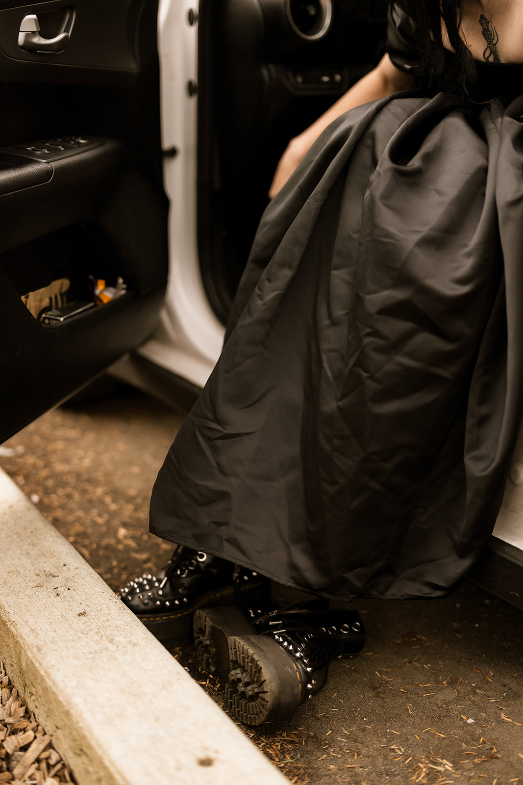A person in a black wedding dress puts on their studded boots, getting ready for their elopement.
