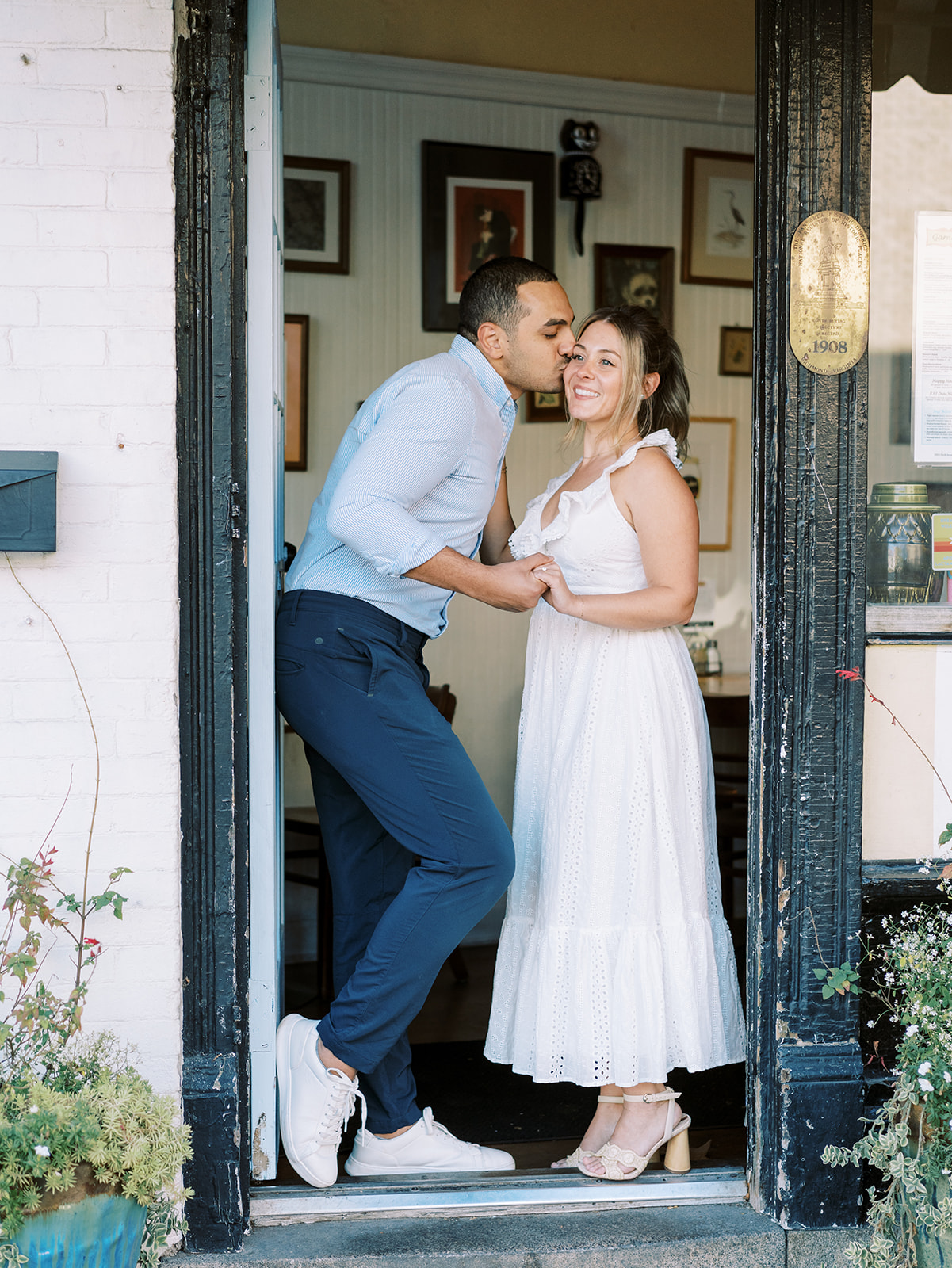 A couple's engagement photo in front of Garnetts Sandwich Shop in Richmond Virginia wearing a white dress in the doorway