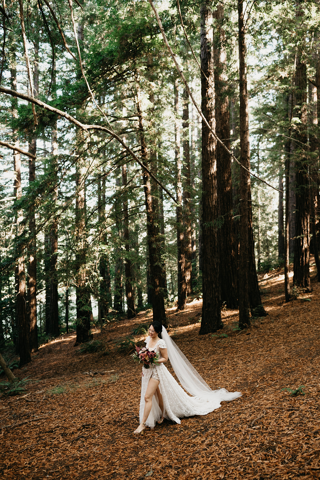 Bride in wedding dress walks to ceremony site in the forest of Big Sur, California.