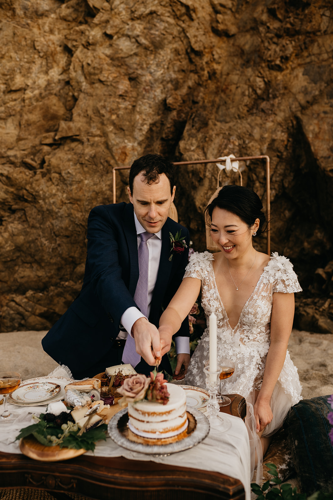 Bride and groom cutting their wedding cake on the beach during their beach picnic in Big Sur California.