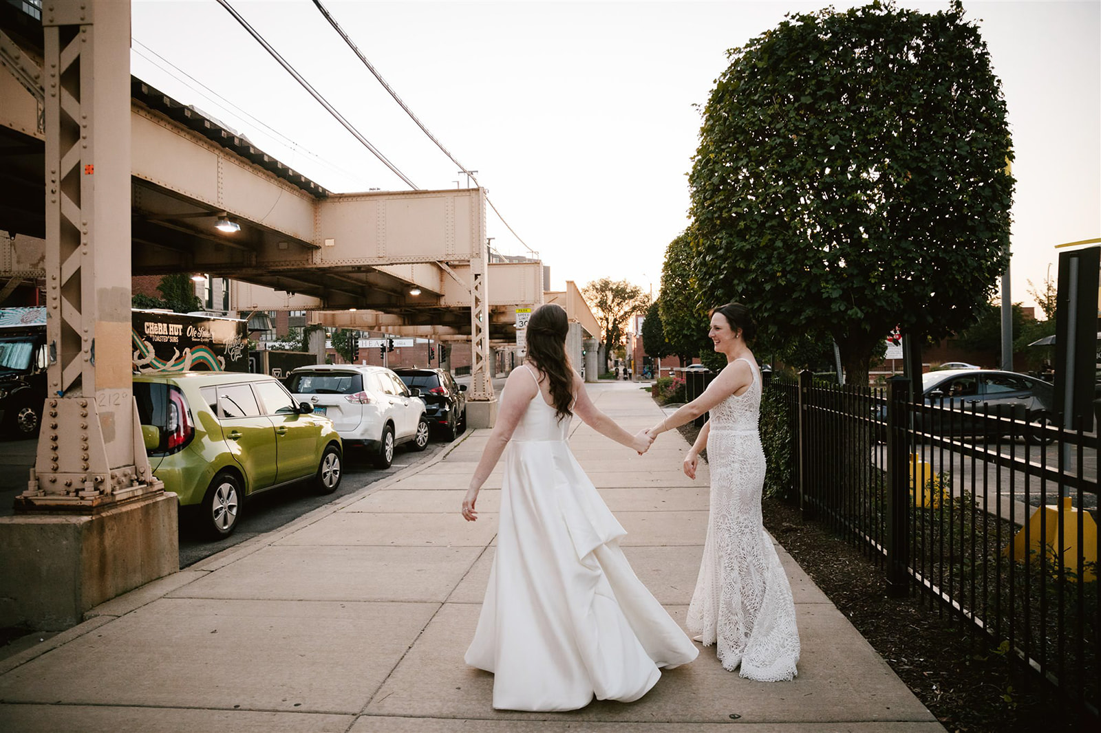 Two brides against a Chicago street at sunset, showcasing the stunning cityscape and their radiant joy on their wedding.