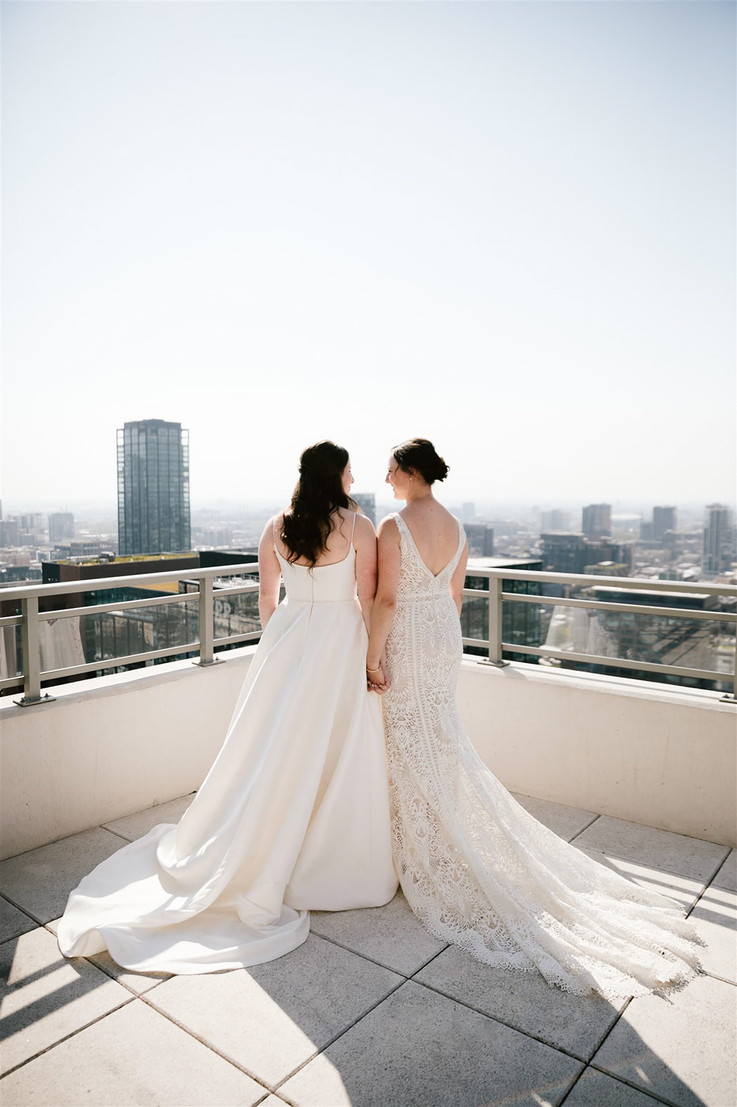 Two brides sharing a first look on Chicago rooftop and skyline backdrop, embracing in a moment of love and anticipation.