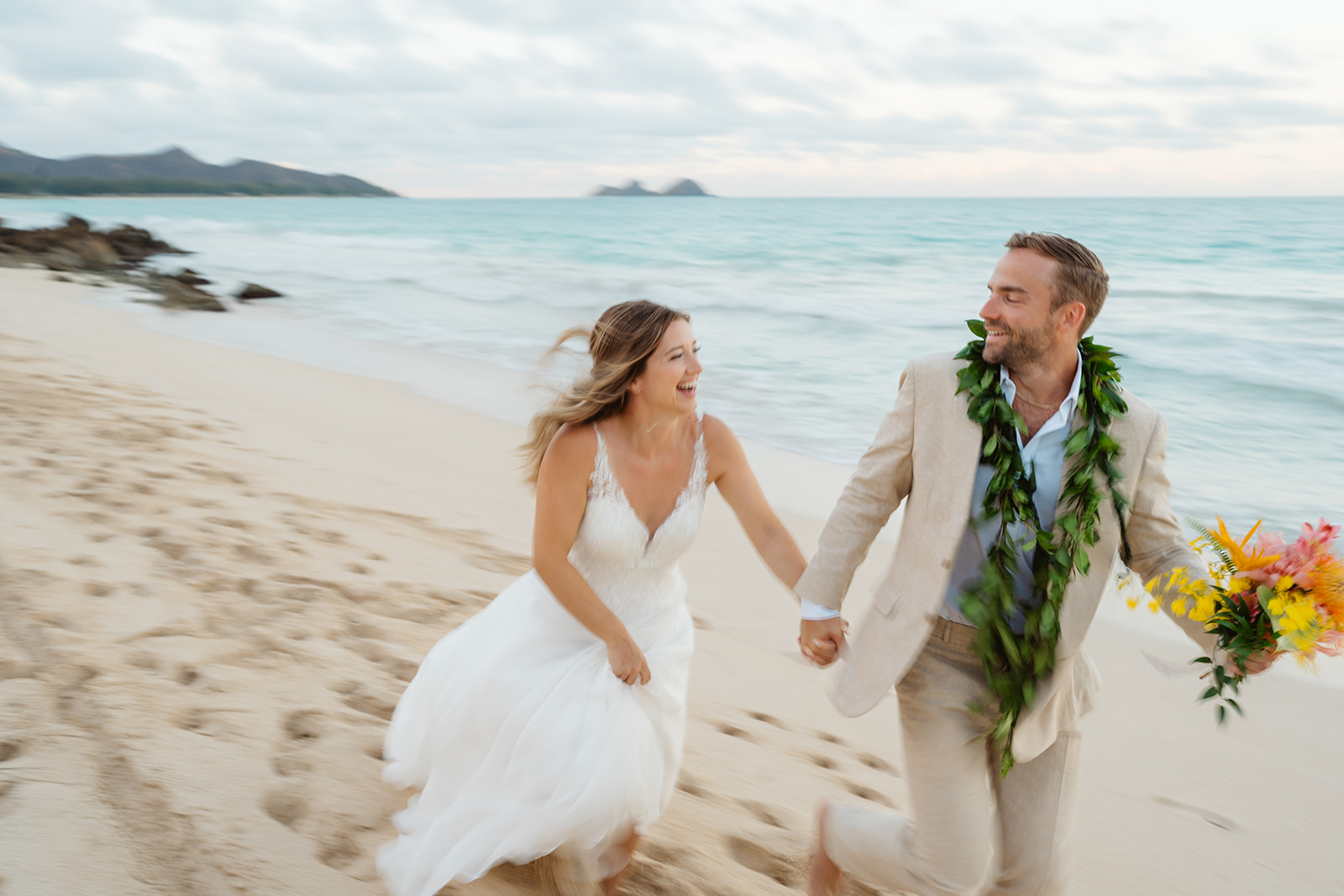 A couple playfully runs along the beach during their oahu wedding