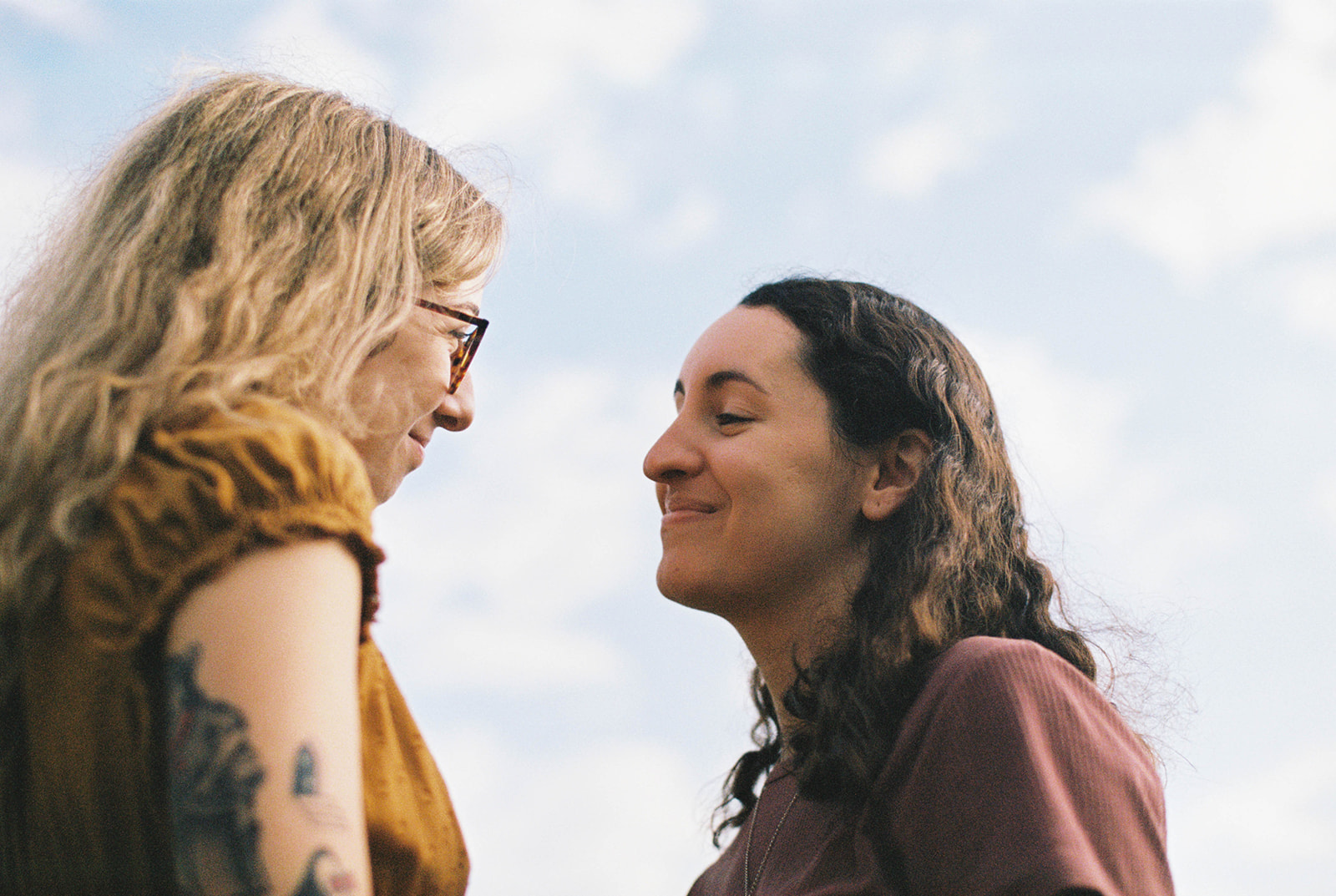 Film photo of LGBTQ+ couple looking at each other with blue sky in background during their engagement session in Atlanta