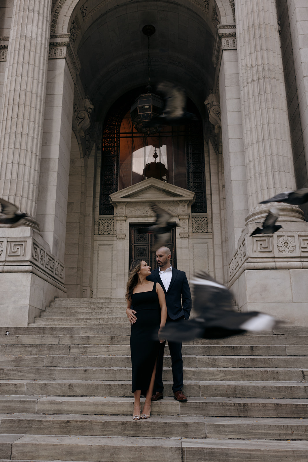 A couple stands on the New York Public Library steps during their engagement session