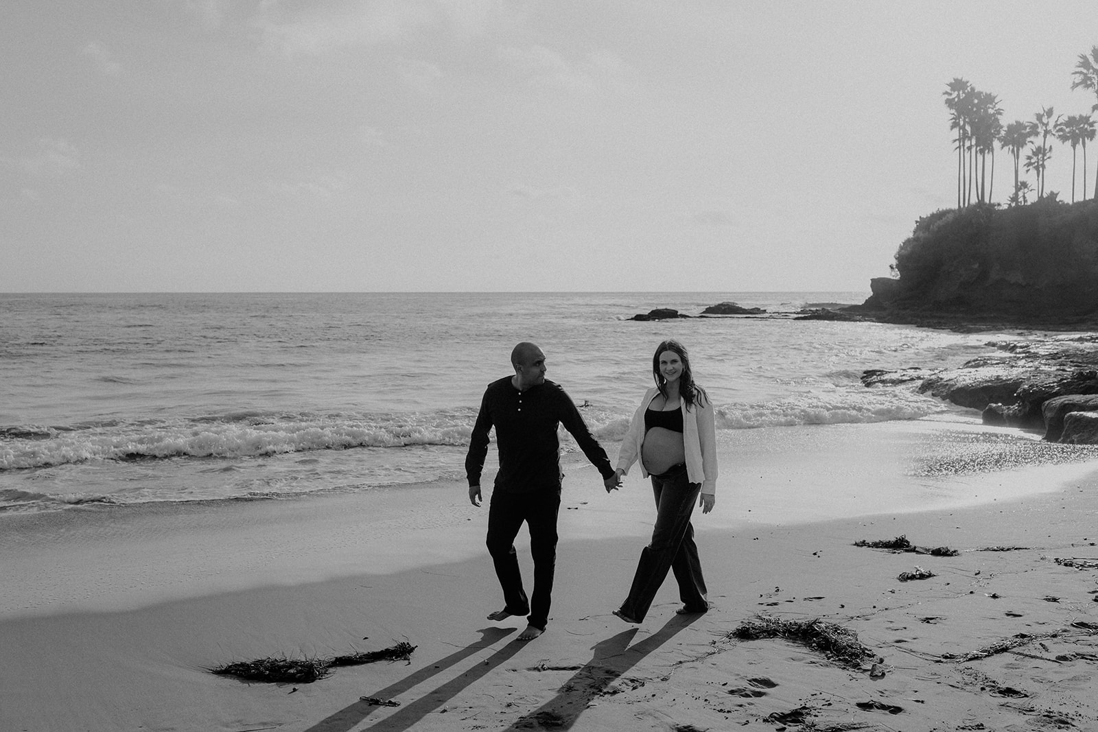 Couple at the beach walking, laguna beach, palm trees behind them, sun in the background, maternity session