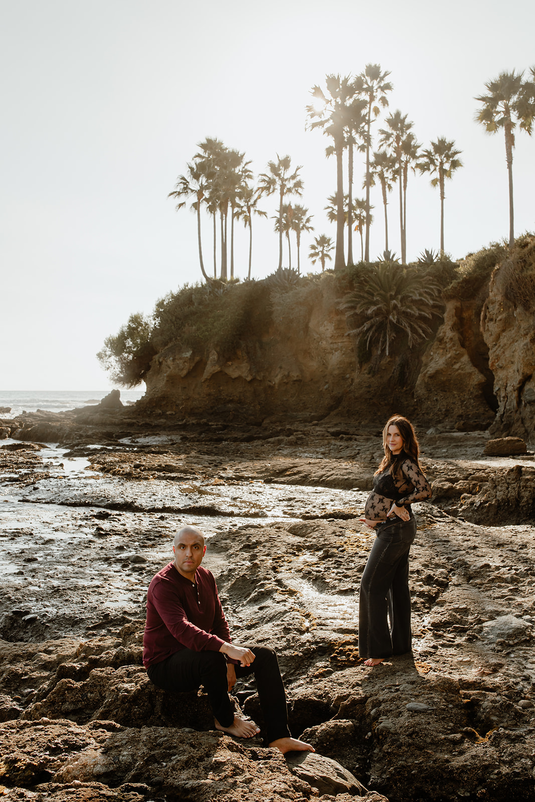 Couple at the beach, laguna beach, palm trees behind them, sun in the background, maternity session