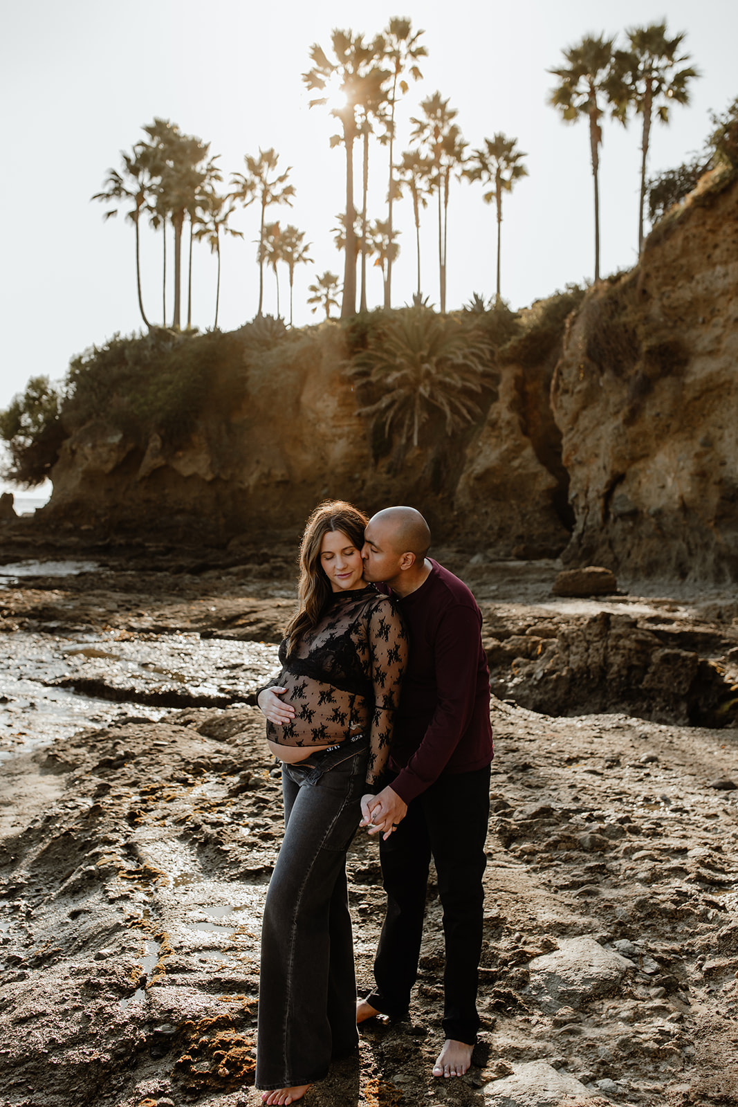 Couple at the beach, laguna beach, palm trees behind them, sun in the background, maternity session
