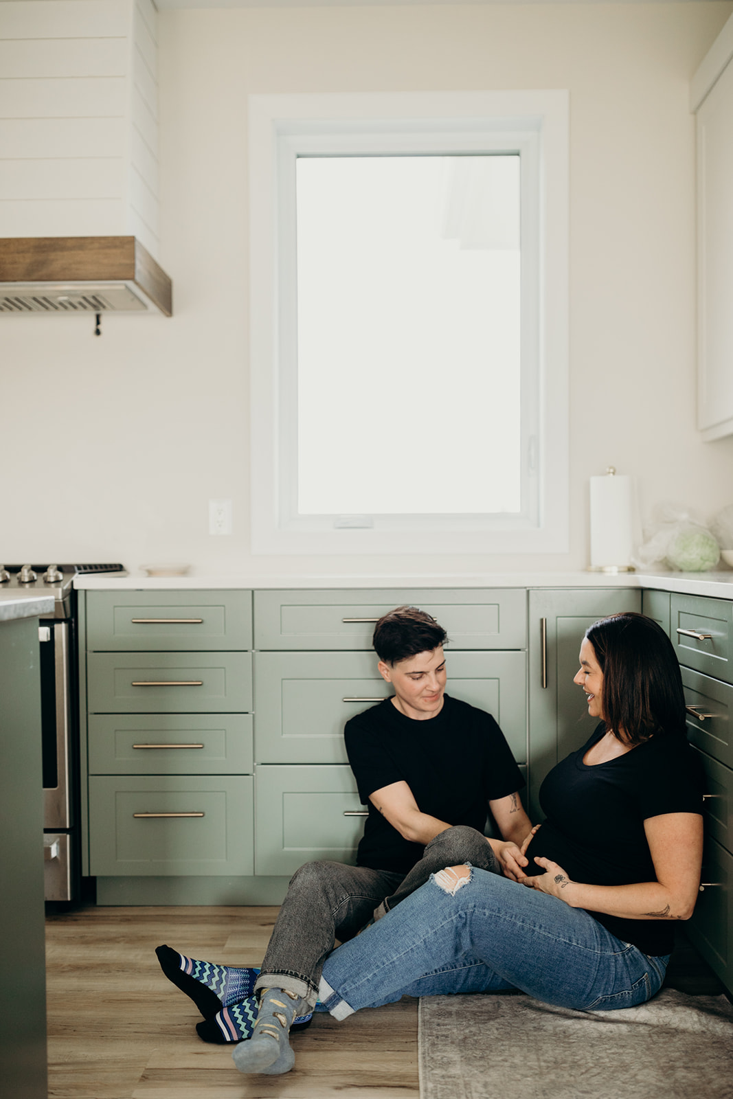 Same sex couple poses in kitchen during their maternity photoshoot 