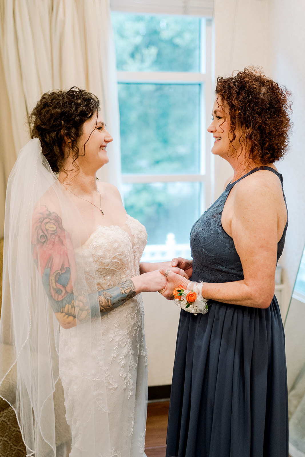 Mother and daughter holding hands in front of window on wedding day