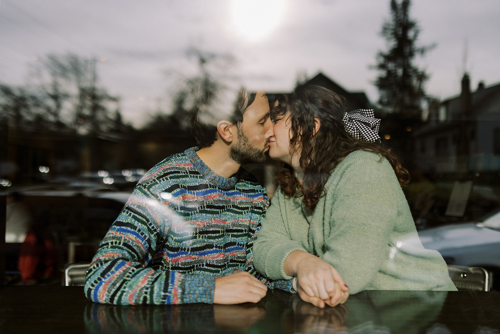 Couple kissing in a coffee shop window during their maternity session in Spokane, Washington.