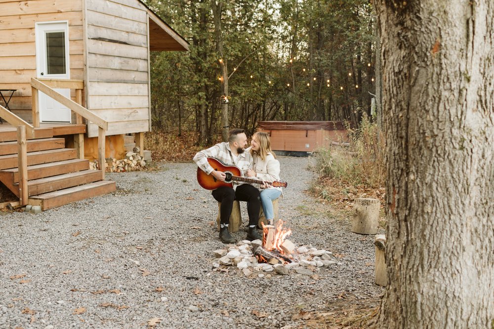 Cabin engagement session playing guitar by the cottage fire