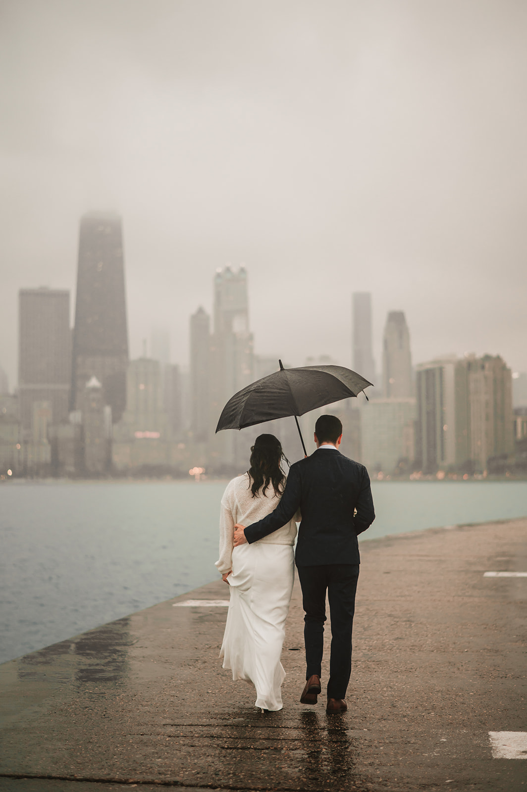 Intimate rainy day Chicago elopement wedding photography - Skyline over lake Michigan, couple walking with an umbrela