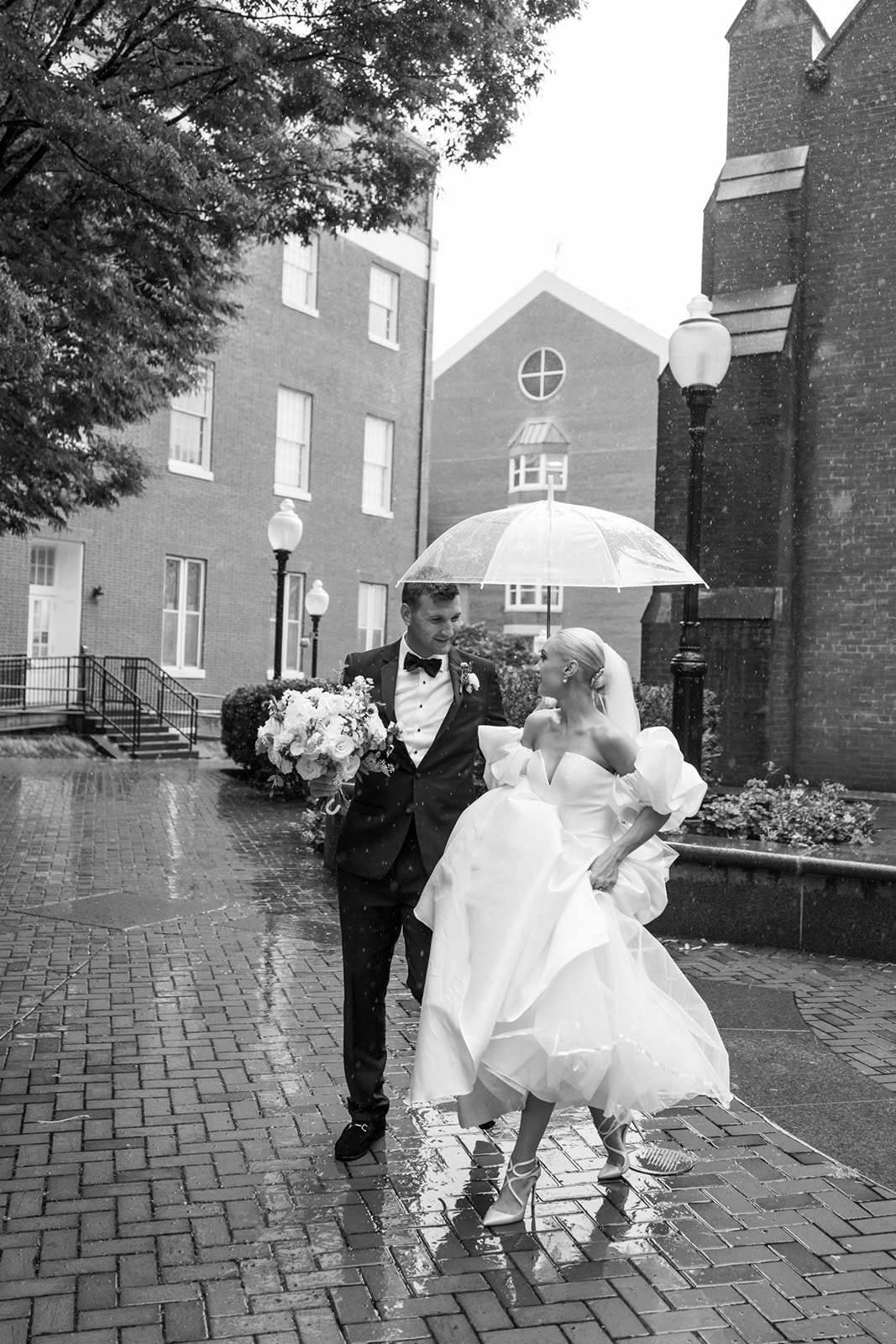 Bride and Groom walk across Georgetown University campus in the rain under an umbrella
