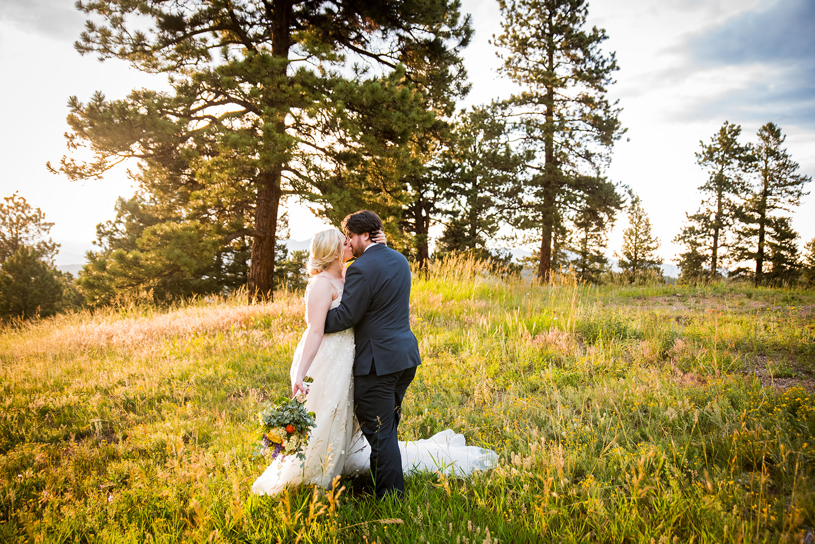 The bride and groom share a kiss in a grassy field at golden hour.