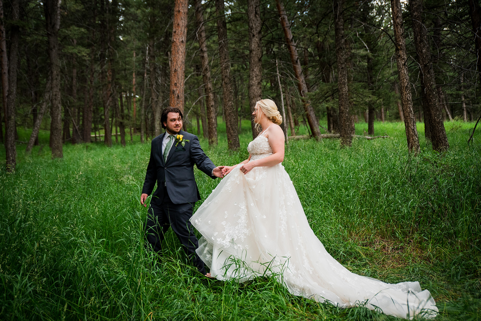 The groom leads the bride as they walk through a grassy field.