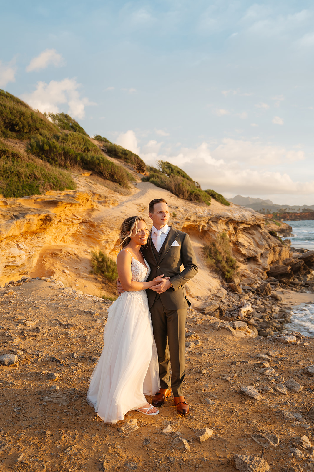 A couple who eloped on Kauai look toward the sunrise on a cliff near Shipwreck beach.