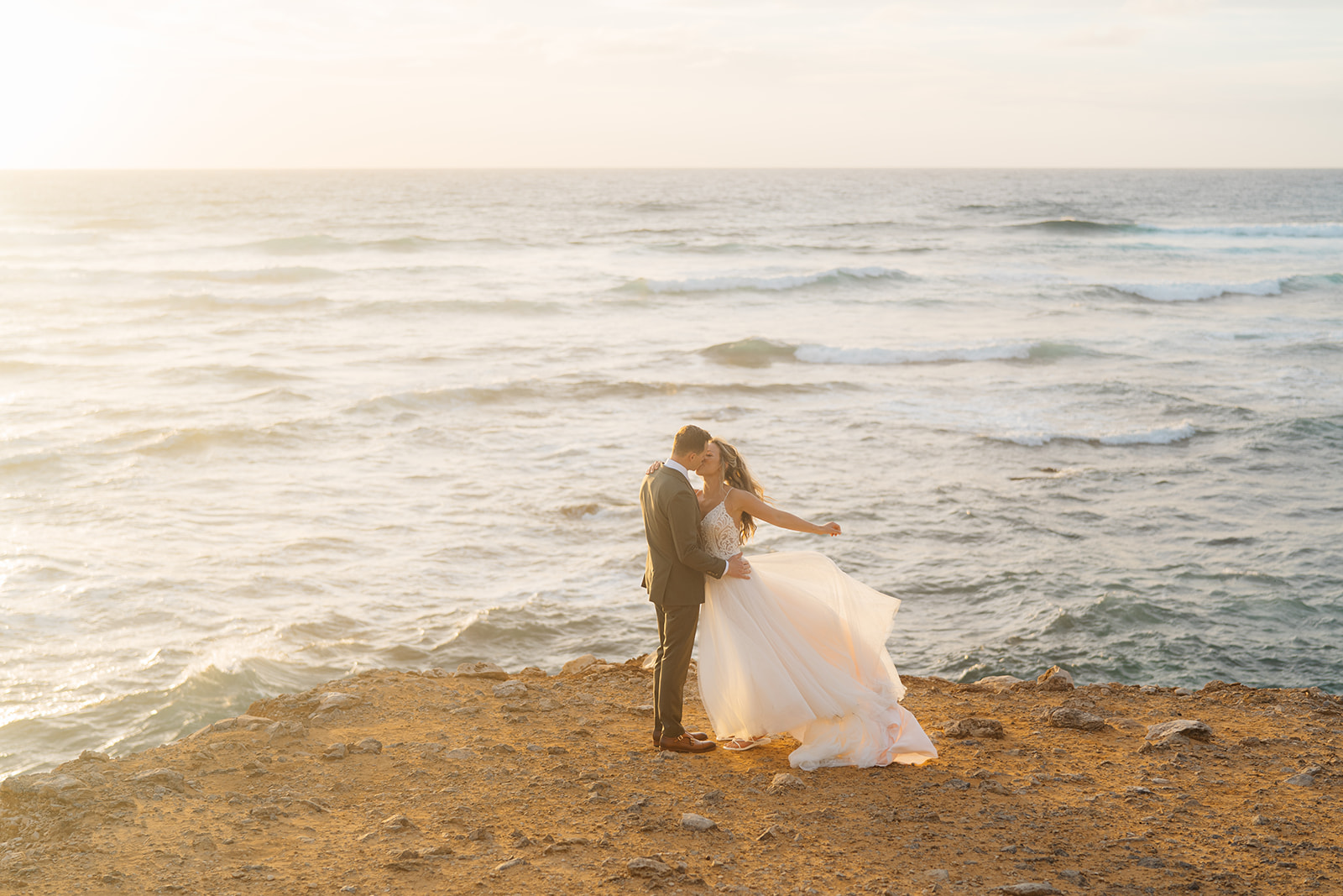A couple who eloped on Kauai kiss on a cliff near Shipwreck beach.