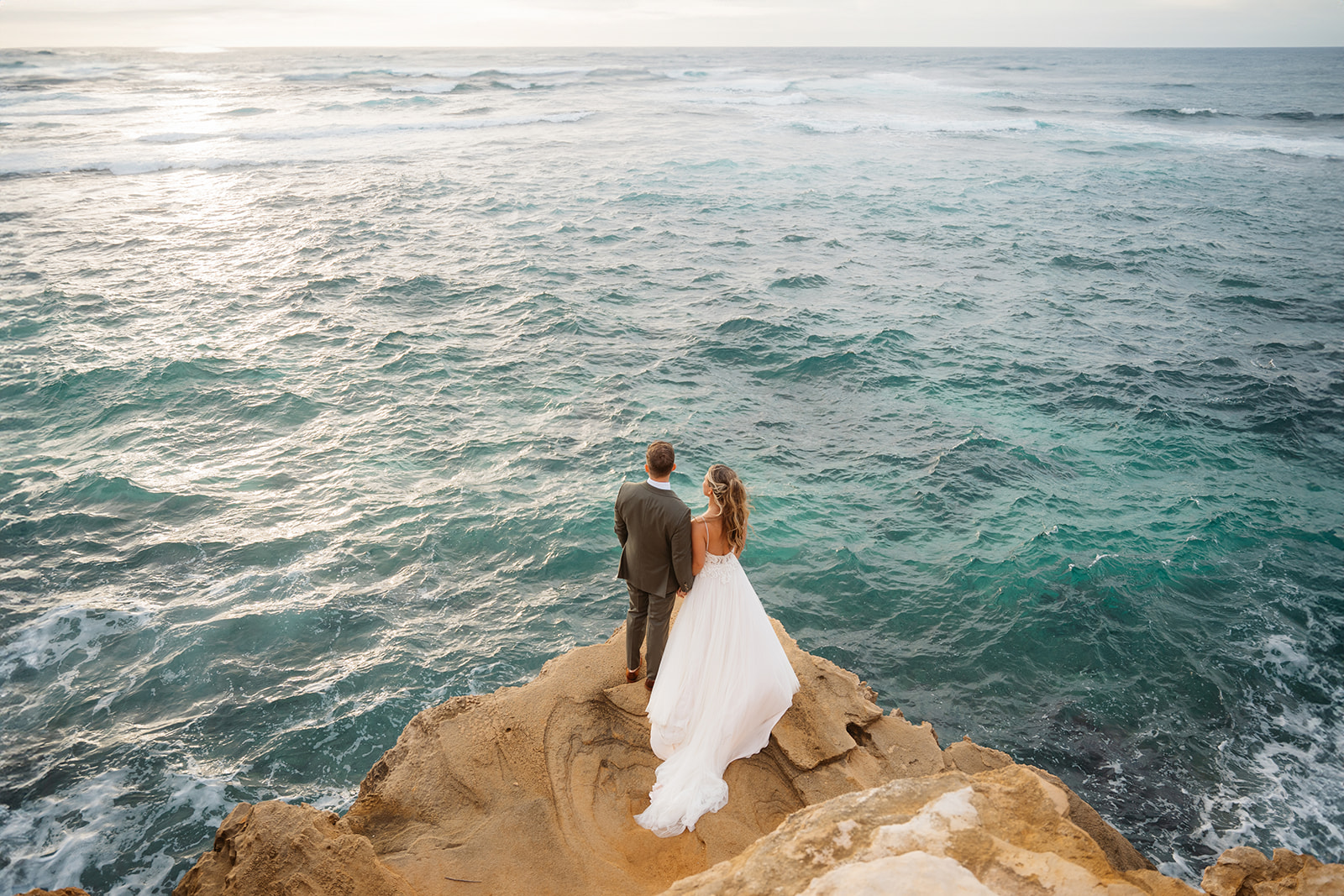 A couple who eloped on Kauai look out at blue water on a cliff near Shipwreck beach.