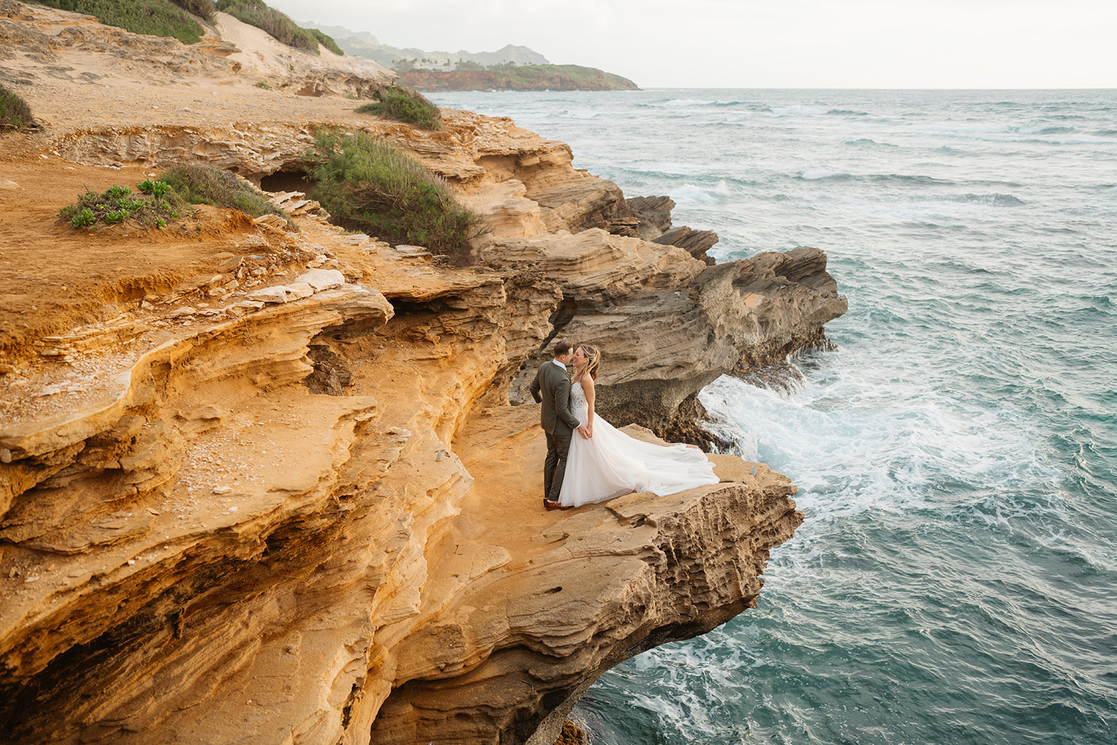 A couple who eloped on Kauai embrace on a cliff near Shipwreck beach.