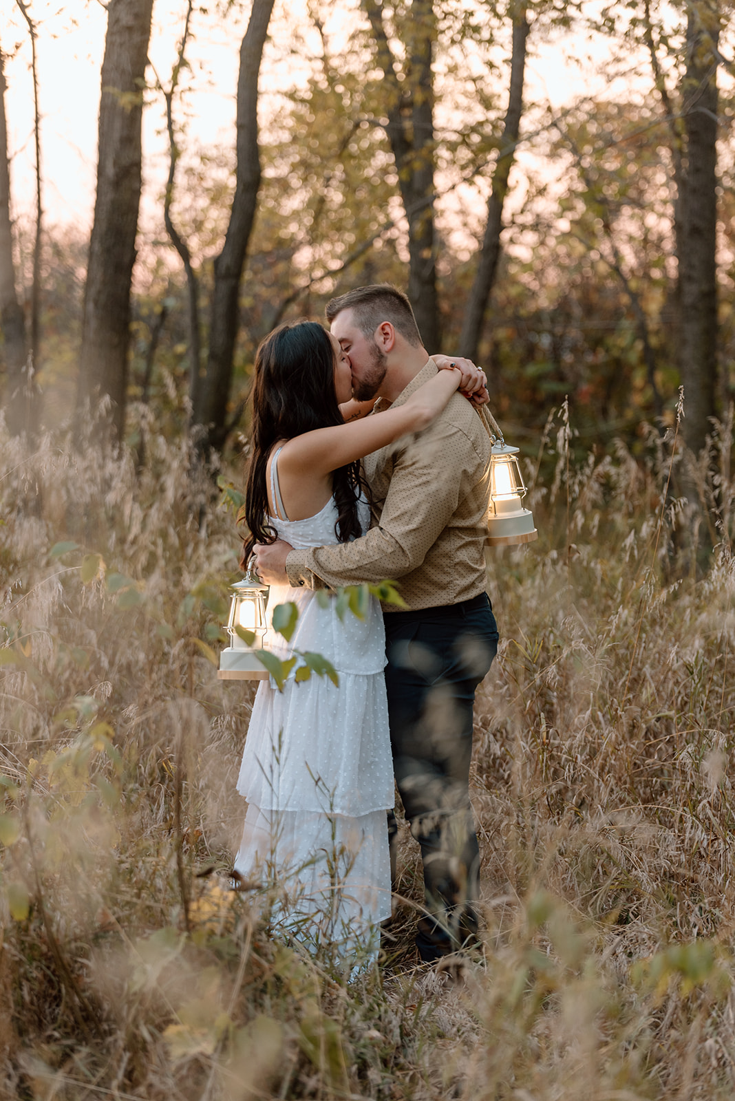 Engaged couple kisses in tall grass in the golden light with langerns