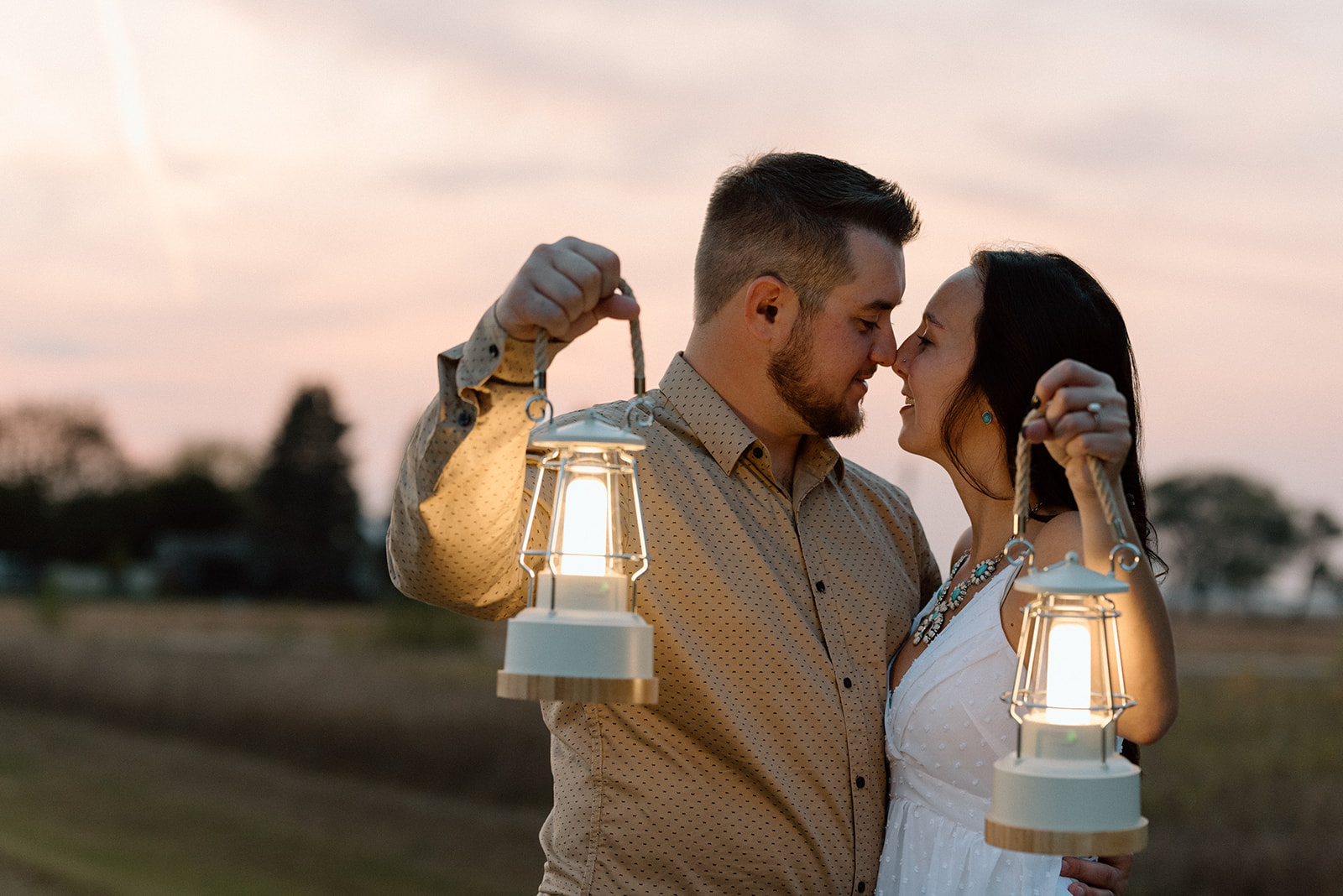Engaged couple snuggles close and holds out their lanterns while the sky lights up behind them