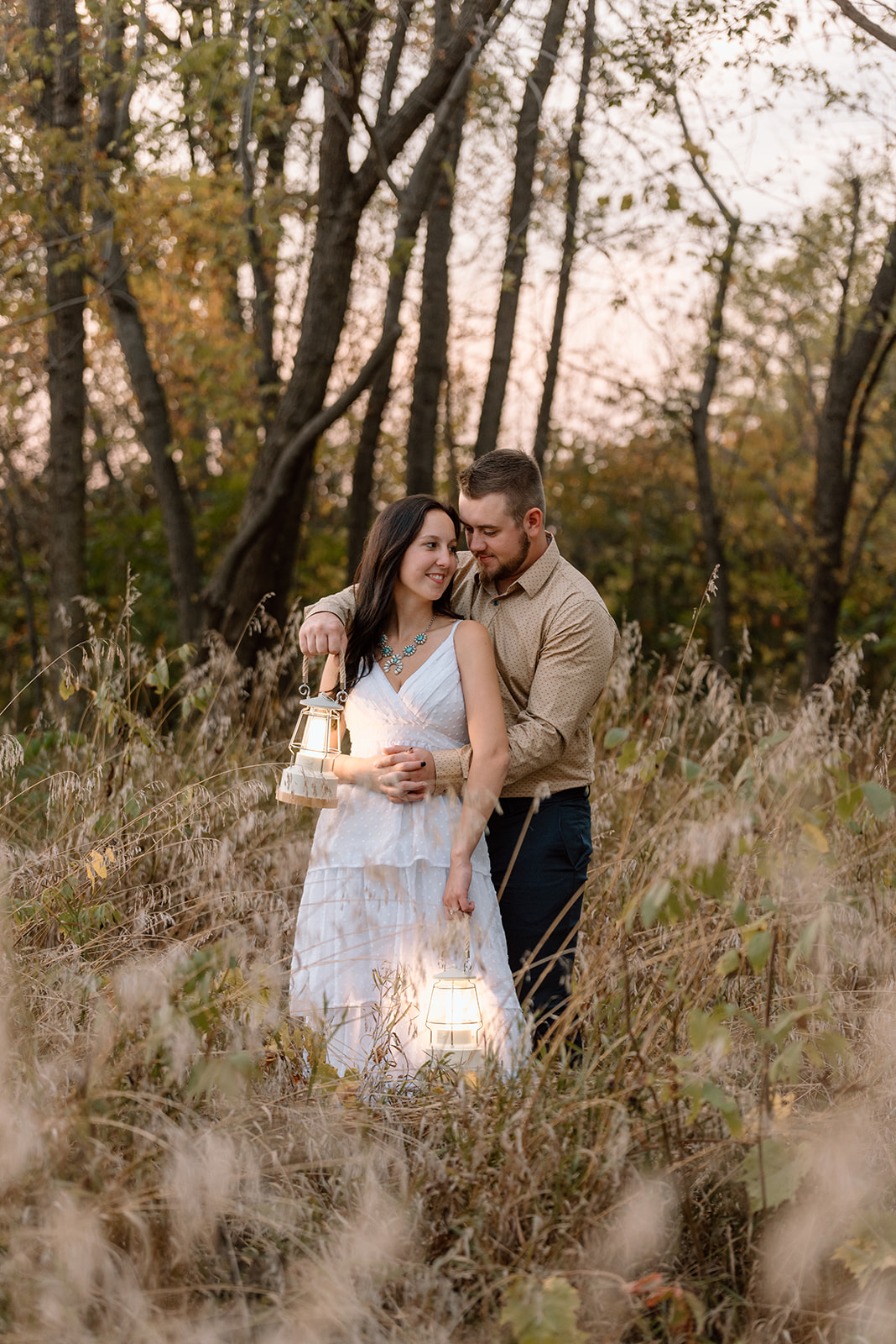 Man embraces woman from behind in the tall grass after sunset with lanterns