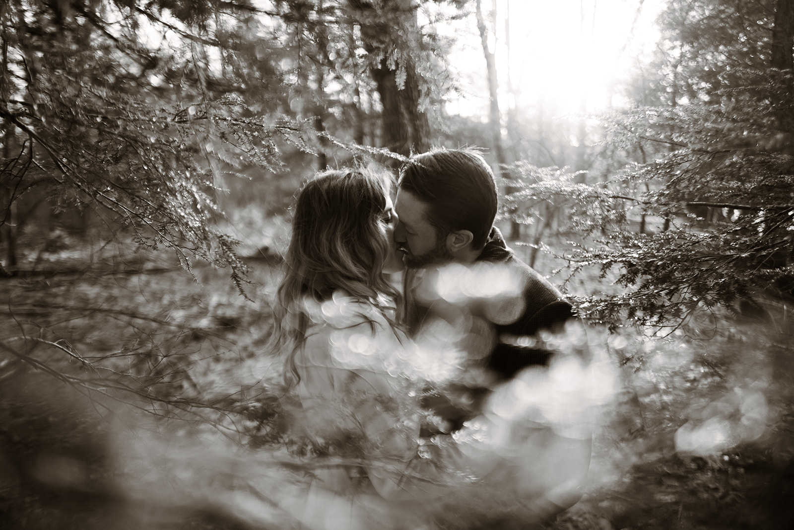 Intimate moment of couple kissing in serene Poconos forest, showcasing natural engagement photography.