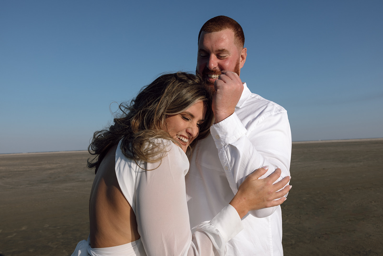 A couple laughs during their engagement session in New Jersey on the beach