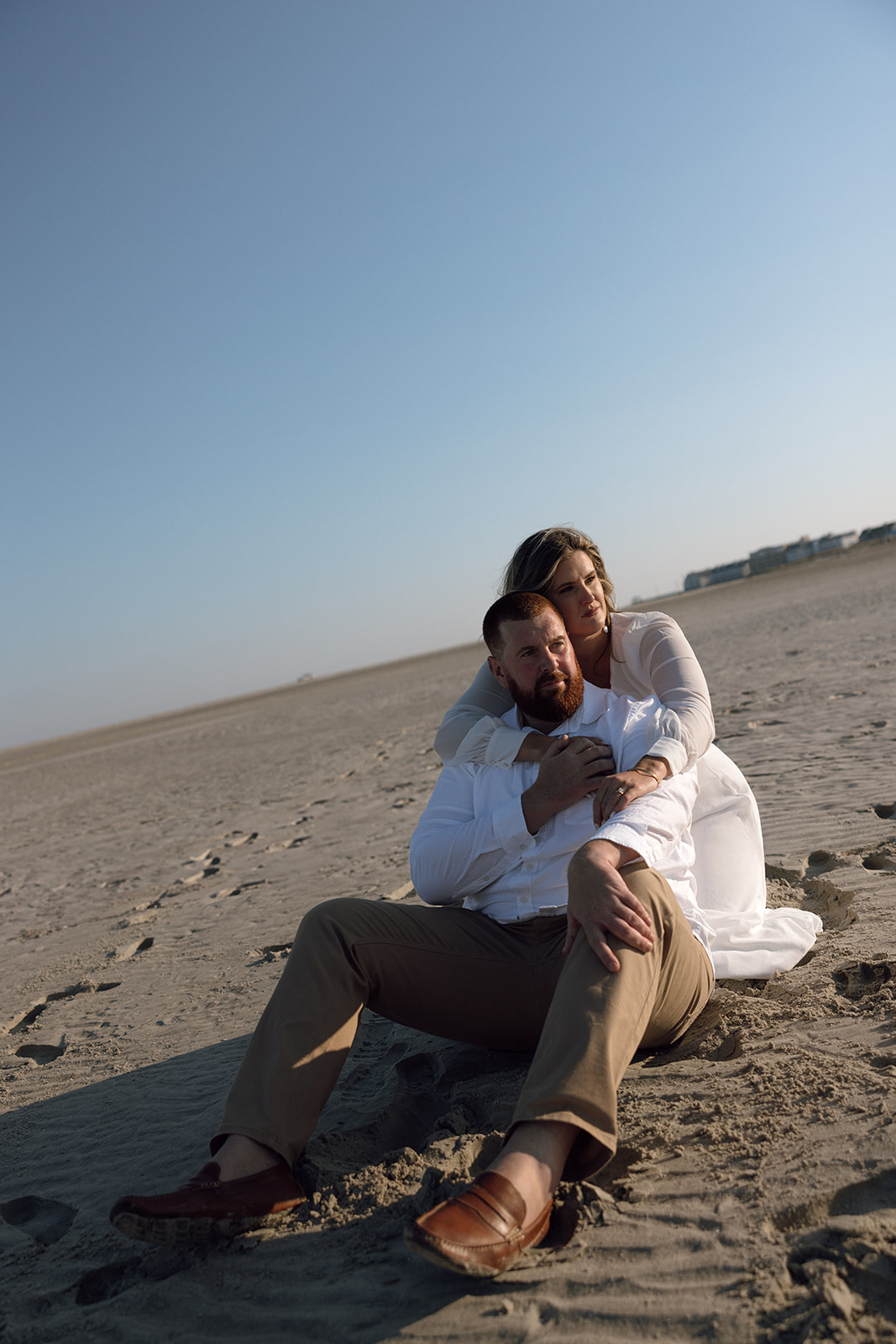 A couple sits on the sand during their engagement session in New Jersey on the beach