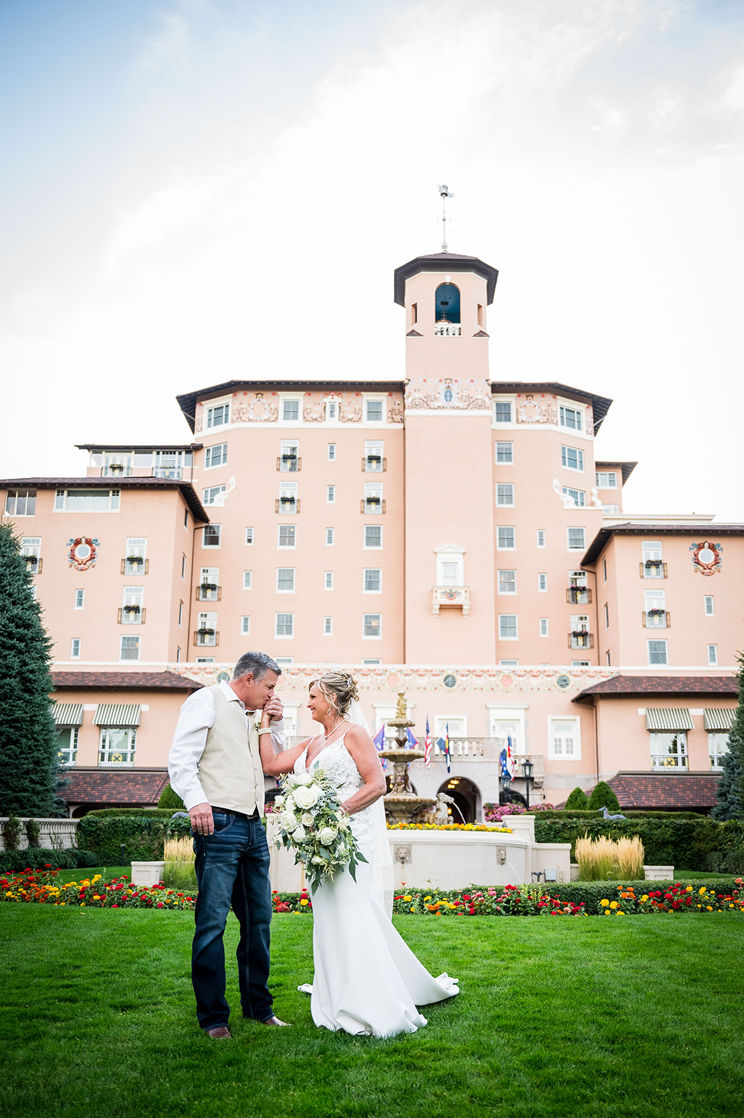 The groom kisses the bride's hand with the Broadmoor Hotel in the background.