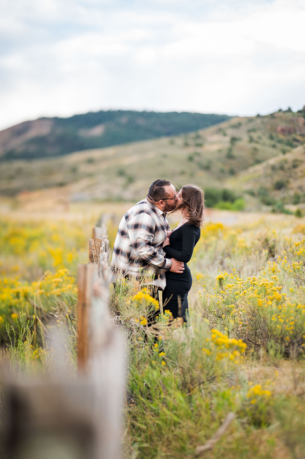 The man and woman lean in for a kiss surrounded by yellow flowers.